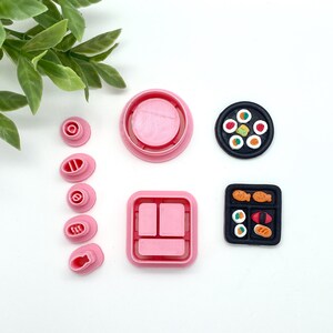 May include: Pink and black polymer clay cutters for making sushi. The set includes a round plate, a square plate, a set of cutters for making sushi rolls, and a set of cutters for making individual pieces of sushi.
