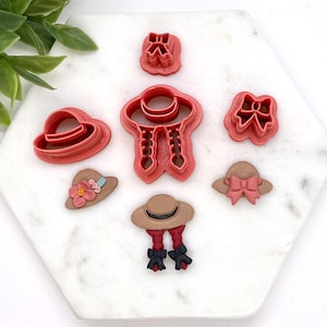 May include: A set of seven red plastic cookie cutters shaped like hats and bows. The cutters are on a white marble surface.