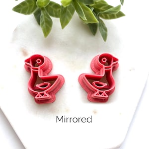 May include: Two pink plastic cookie cutters shaped like ducks, positioned side by side. One duck faces left and the other faces right, creating a mirrored pair. The word Mirrored is printed in black text below the two cookie cutters.