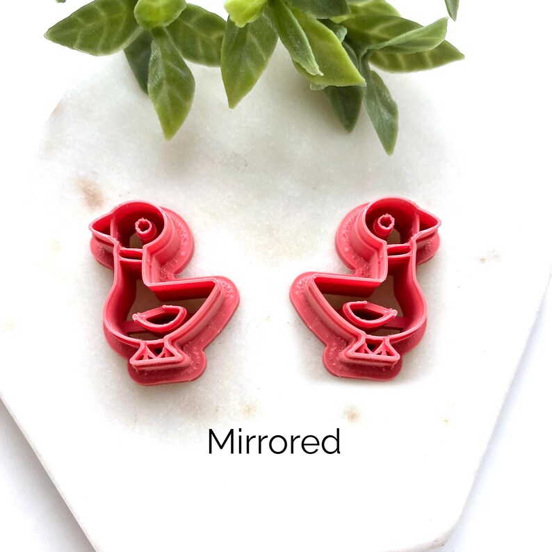 May include: Two pink plastic cookie cutters shaped like ducks, positioned side by side. One duck faces left and the other faces right, creating a mirrored pair. The word Mirrored is printed in black text below the two cookie cutters.