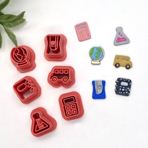 May include: A set of ten red plastic cookie cutters shaped like school supplies, including a globe, a bus, a calculator, a pencil sharpener, a beaker, and a notebook.