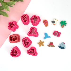 May include: A set of 15 pink plastic cookie cutters shaped like various summer-themed objects, including a flip-flop, a palm tree, a seagull, a camera, a starfish, a sailboat, a hat, a mermaid tail, and a seashell.