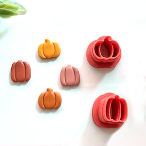 May include: Four orange, pink, and brown pumpkin-shaped clay ornaments and two red plastic pumpkin cookie cutters.