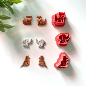 May include: Set of six red plastic cookie cutters shaped like a fox, elephant, and kangaroo.  The cutters are shown next to brown and white clay animal shapes.