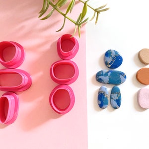 May include: Set of pink polymer clay cutters and five different polymer clay shapes. The shapes are blue with gold flecks, brown, orange, and pink.