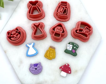 May include: A set of 10 red, purple, blue, green, and yellow plastic cookie cutters shaped like Alice in Wonderland characters and objects. The cutters include a Cheshire Cat, a Mad Hatter, a mushroom, a bottle, a dress, and a playing card.