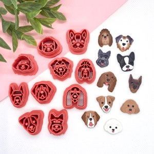 May include: A set of 18 pink plastic dog-shaped cookie cutters. The cutters are arranged in a semi-circle on a pink and white background.