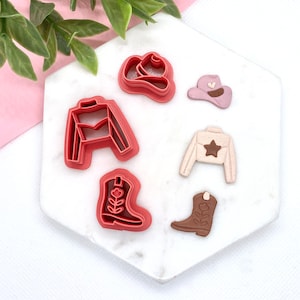 May include: Set of six red and brown plastic cookie cutters shaped like cowboy boots, a cowboy hat, and a vest. The cutters are on a white marble surface.