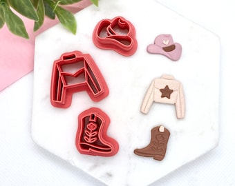 May include: Set of six red and brown plastic cookie cutters shaped like cowboy boots, a cowboy hat, and a vest. The cutters are on a white marble surface.