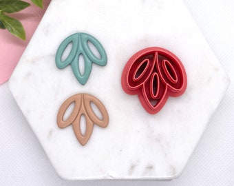 May include: Three plastic cookie cutters in the shape of a leaf. The cutters are teal, brown, and red.
