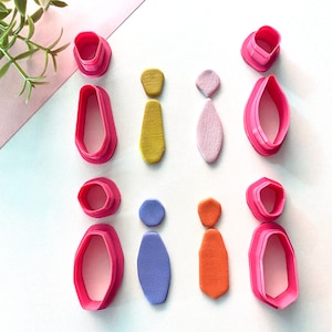 May include: A set of six pink plastic cookie cutters in various shapes, including a tie, a circle, and a hexagon. The cutters are arranged in three rows of two, with a sample of each shape made from colourful clay next to each cutter.