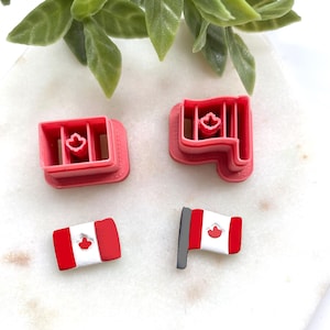 May include: Four red and white Canadian flag-themed items. Two are cookie cutters, and two are flag-shaped charms. The cookie cutters are rectangular and flag-shaped. The charms are miniature flags with a grey pole.