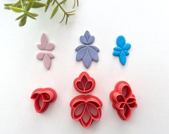 May include: Set of six red and blue plastic cookie cutters shaped like flowers. The cutters are arranged on a white surface.