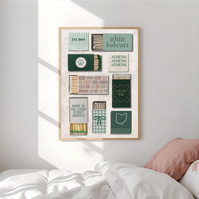 Puede incluir: Una impresi&oacute;n enmarcada con dise&ntilde;os de cajas de cerillas en tonos verdes, beige y blanco. Las cajas de cerillas muestran textos como "Ohio Bobcats", "Athens" y "Home of the Court Street Shuffle". La obra de arte se exhibe sobre un fondo blanco.