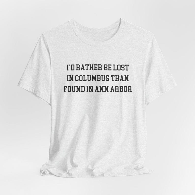May include: A light gray t-shirt with the text "I'D RATHER BE LOST IN COLUMBUS THAN FOUND IN ANN ARBOR" in black, centered on the front. The shirt has a crew neck and short sleeves.