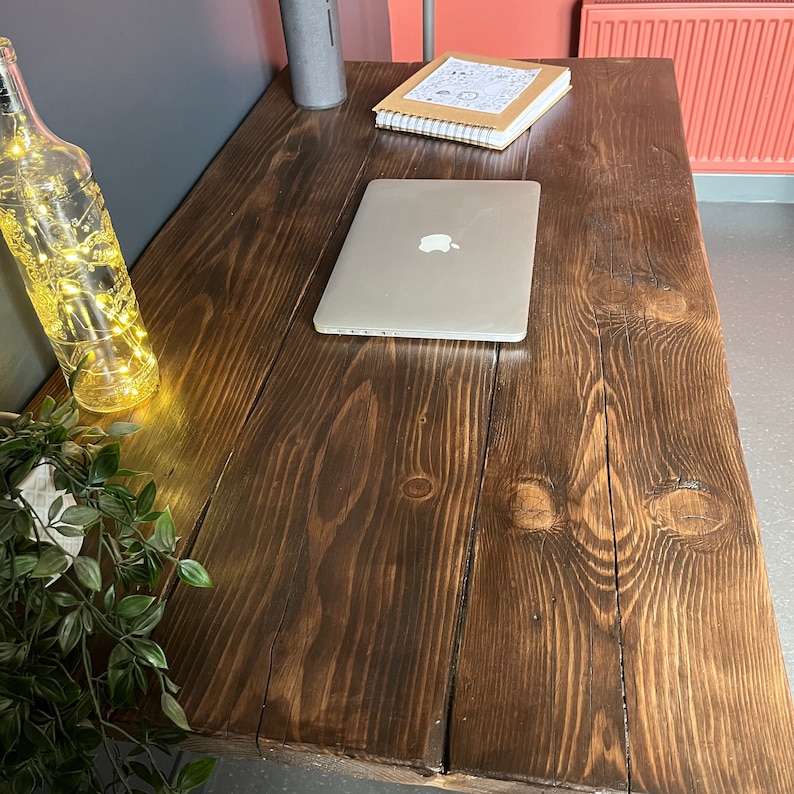 K&ouml;nnte beinhalten: Ein dunkelbrauner Holztisch mit einem Laptop, einem Notizbuch und einer durchsichtigen Glasflasche mit Lichtern darin. Der Tisch hat ein rustikales, wiederverwendetes Holz-Design.