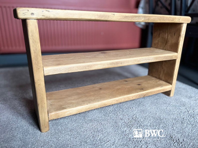 May include: A wooden shoe rack with two shelves. The rack is made of natural wood with a light brown finish. It has a simple design with straight lines and a rectangular shape.
