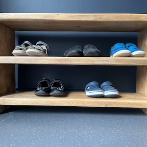 May include: A wooden shoe rack with two shelves. The top shelf has three pairs of sandals and two pairs of black shoes. The bottom shelf has two pairs of blue shoes.