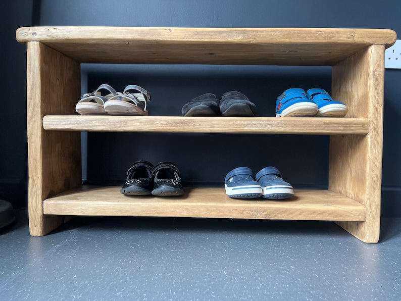 May include: A wooden shoe rack with two shelves. The top shelf has three pairs of sandals and two pairs of black shoes. The bottom shelf has two pairs of blue shoes.