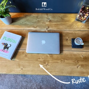 K&ouml;nnte beinhalten: Ein rustikaler Schreibtisch aus Kiefernholz mit einem Laptop, einem Buch mit dem Titel "Another Year at Plumdog" von Emma Chichester Clark und einer Tasse auf einem Schieferuntersetzer. Der Schreibtisch ist aus Naturholz mit einer hellbraunen Oberfl&auml;che.
