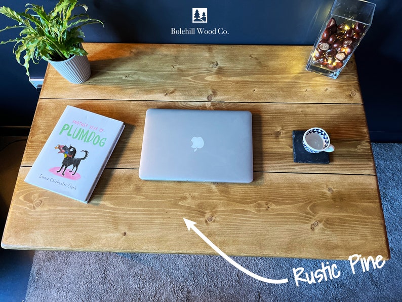 K&ouml;nnte beinhalten: Ein rustikaler Schreibtisch aus Kiefernholz mit einem Laptop, einem Buch mit dem Titel "Another Year at Plumdog" von Emma Chichester Clark und einer Tasse auf einem Schieferuntersetzer. Der Schreibtisch ist aus Naturholz mit einer hellbraunen Oberfl&auml;che.