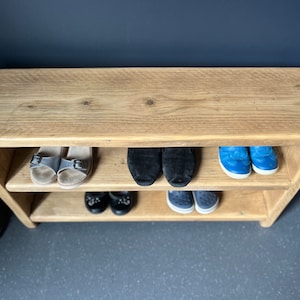 May include: A wooden shoe rack with two shelves. The top shelf is empty and the bottom two shelves are filled with shoes. The shoes include sandals, sneakers, and loafers.