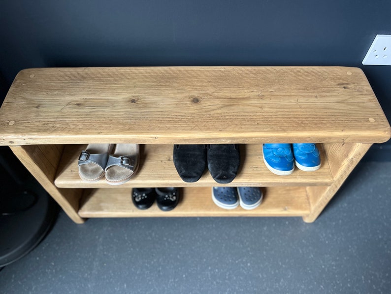 May include: A wooden shoe rack with two shelves. The top shelf is empty and the bottom two shelves are filled with shoes. The shoes include sandals, sneakers, and loafers.