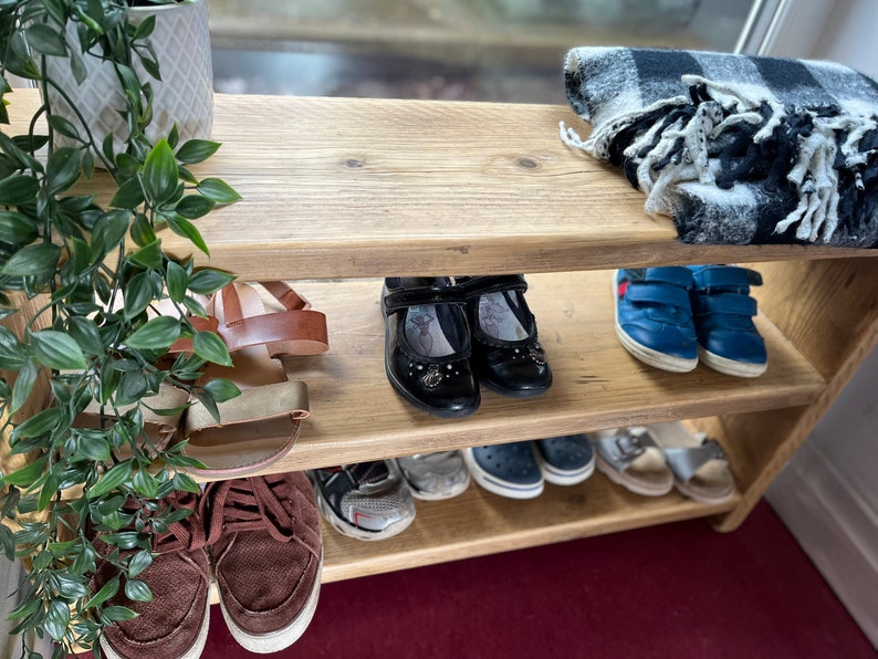 May include: A wooden shoe rack with three shelves. The top shelf has a black and white plaid throw blanket. The middle shelf has a pair of brown sandals, a pair of black flats, and a pair of blue sneakers. The bottom shelf has a pair of brown sneakers, a pair of black sandals, and a pair of blue sandals.
