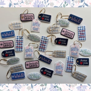 May include: A collection of embroidered keychains in various shapes, featuring religious phrases like "Jesus Saves," "God is Good," and "Love like Jesus." The keychains have gold-colored metal rings and are in shades of blue, pink, and white.