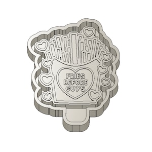 Puede incluir: Un cortador de galletas blanco con forma de contenedor de patatas fritas con el texto "FRIES BEFORE GUYS" dentro de un corazón. El contenedor está lleno de patatas fritas y rodeado de pequeños corazones.