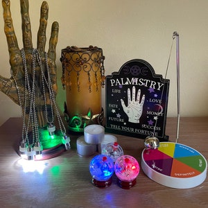 May include: A collection of fortune-telling tools, including a palmistry sign, pendulum, and light-up crystal balls. The palmistry sign reads "Palmistry, Life, Love, Fate, Future, Success, Tell Your Fortune." A color wheel reads "Maybe, Definitely, No Way."
