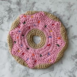 May include: A pink crocheted donut with brown frosting and colorful sprinkles.