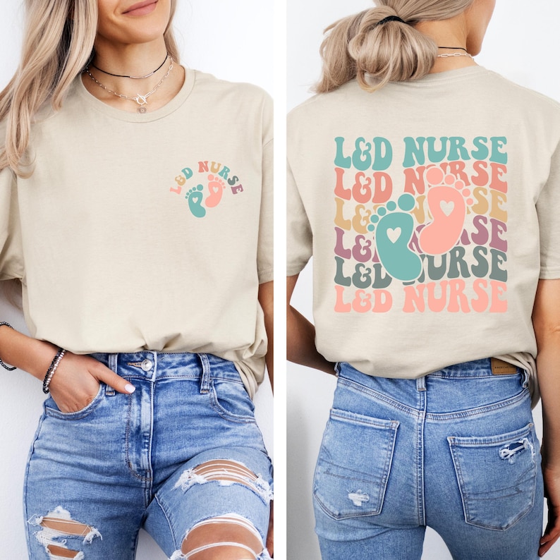 May include: A beige t-shirt with a graphic of a pair of baby footprints and the text "L&D NURSE" on the front. The back of the shirt has the text "L&D NURSE" repeated in a rainbow pattern with a heart in the middle of each graphic.