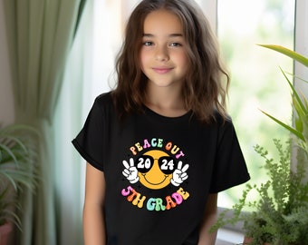 May include: Black t-shirt with a yellow smiley face wearing sunglasses and the text "Peace Out 5th Grade 2024" in rainbow colors.