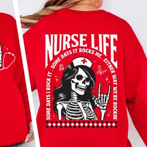 May include: Red sweatshirt with a white graphic that says "NURSE LIFE" with a skeleton wearing a nurse's cap and the text "SOME DAYS I ROCK IT. SOME DAYS IT ROCKS ME. EITHER WAY WE'RE ROCKIN'".