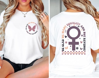 Puede incluir: Camiseta blanca con una mariposa rosa y el texto "Be glad we want equality and not revenge" en la parte delantera. La parte posterior de la camiseta tiene un símbolo femenino rosa con el texto "Be glad we want equality and not revenge" alrededor.