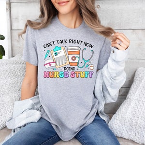 May include: Gray t-shirt with the text "Can't talk right now doing nurse stuff" and a graphic of a stethoscope, coffee cup, thermometer, and a clipboard.
