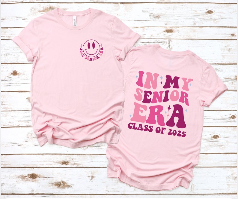Puede incluir: Camiseta rosa con un gr&aacute;fico de cara sonriente en la parte delantera y el texto "In My Senior Era Class of 2025" en la parte posterior.