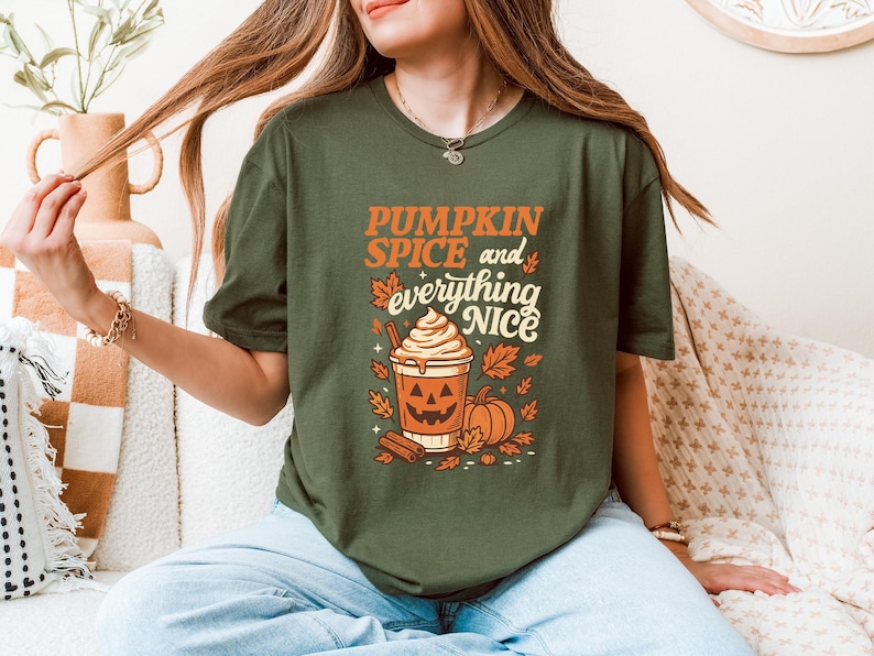 Może przedstawiać: Zielona koszulka z oliwkowym nadrukiem z napisem "PUMPKIN SPICE and everything NICE" w kolorze pomarańczowym i białym. Grafika zawiera pumpkin spice latte, dynie i jesienne liście. Koszulka ma okrągły dekolt.