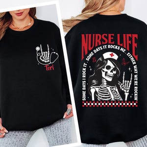 May include: Black sweatshirt with a white skeleton hand design and a stethoscope. The text "Tori" is below the design. The back of the sweatshirt has a nurse skeleton graphic with the words "Nurse Life" and "Some days it rocks me. Either way we're rockin'."