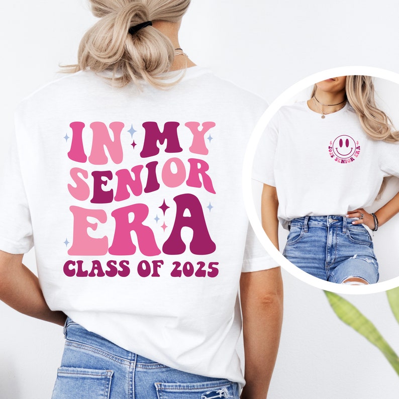 Puede incluir: Camiseta blanca con texto rosa y morado que dice "In My Senior Era Class of 2025". Una segunda camiseta blanca con una cara sonriente rosa y el texto "2025 Senior Era" se muestra en el fondo.