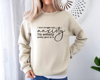 Puede incluir: Una sudadera beige con texto negro que dice "No lucho con la ansiedad, en realidad soy bastante buena en eso"