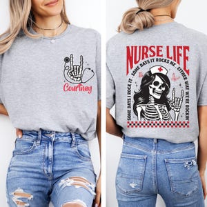 May include: A heather gray t-shirt with a skeleton hand and stethoscope graphic, the name "Courtney" in red script. The back features a "Nurse Life" design with a skeleton nurse and the text "Some days I rock it, either way we're rockin'."