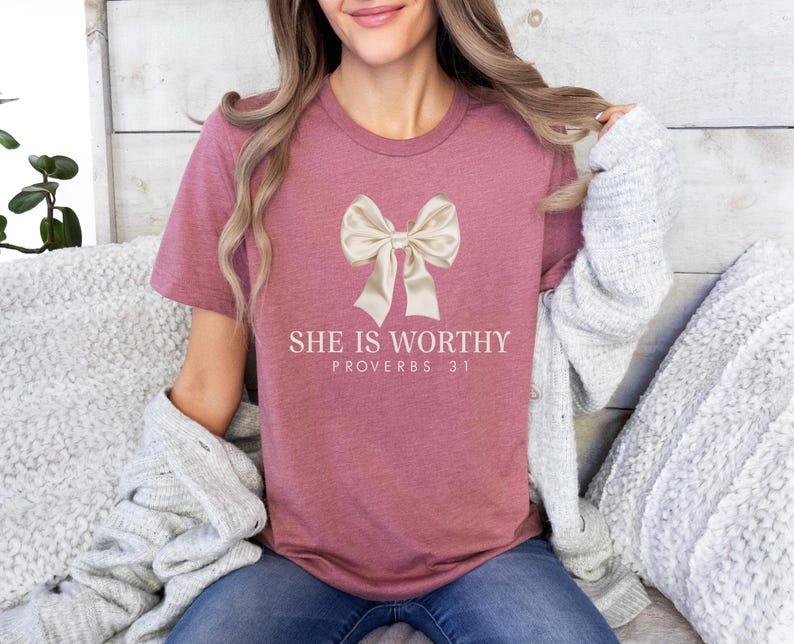 May include: A mauve t-shirt with a large white bow and the text "She is Worthy Proverbs 31" printed on the front.