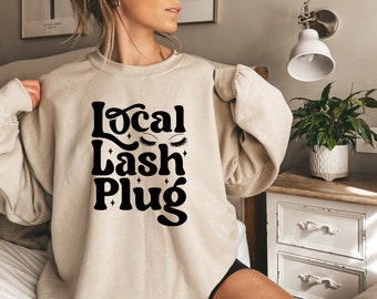 May include: A beige sweatshirt with the text "Local Lash Plug" in black, featuring stylized eyelashes and stars.