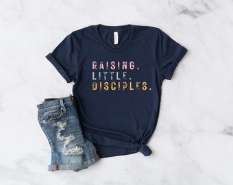 May include: A navy blue t-shirt with the text "RAISING. LITTLE. DISCIPLES." in a retro font with pink, blue, and yellow accents.