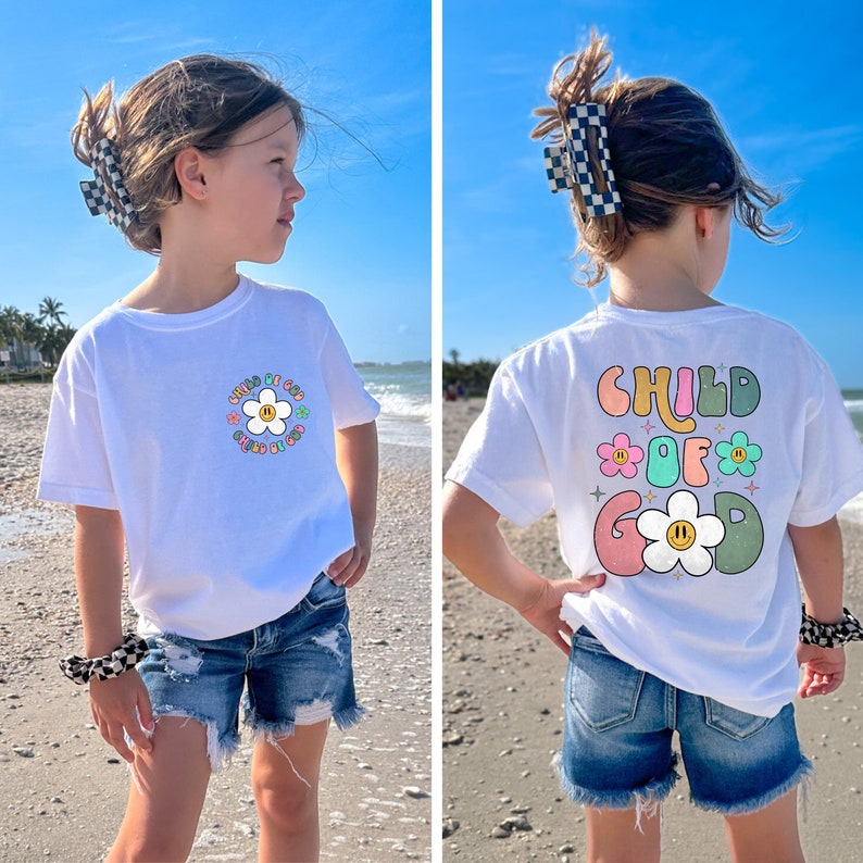 May include: White t-shirt with a colorful graphic of a daisy and the text "Child of God" on the front. The back of the shirt has a similar graphic with the text "Child of God" in a rainbow color scheme.
