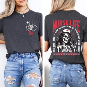 May include: Dark gray t-shirt with a skeleton hand holding a stethoscope and the name "Tim" in red. The back of the shirt features a skeleton nurse graphic with the words "Nurse Life" and "Some days I rock it. Either way we're rockin'."