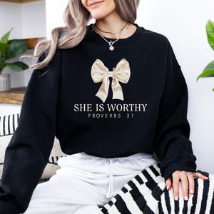May include: Black sweatshirt with a gold bow and the text "She is worthy Proverbs 31" printed on the front.
