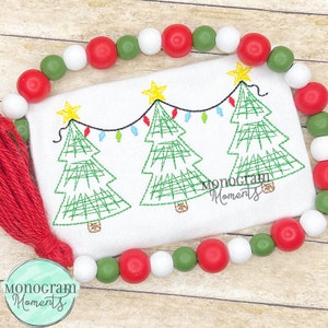 May include: Embroidered design of three green Christmas trees with yellow stars and colorful lights. The design is on a white fabric with a red tassel.